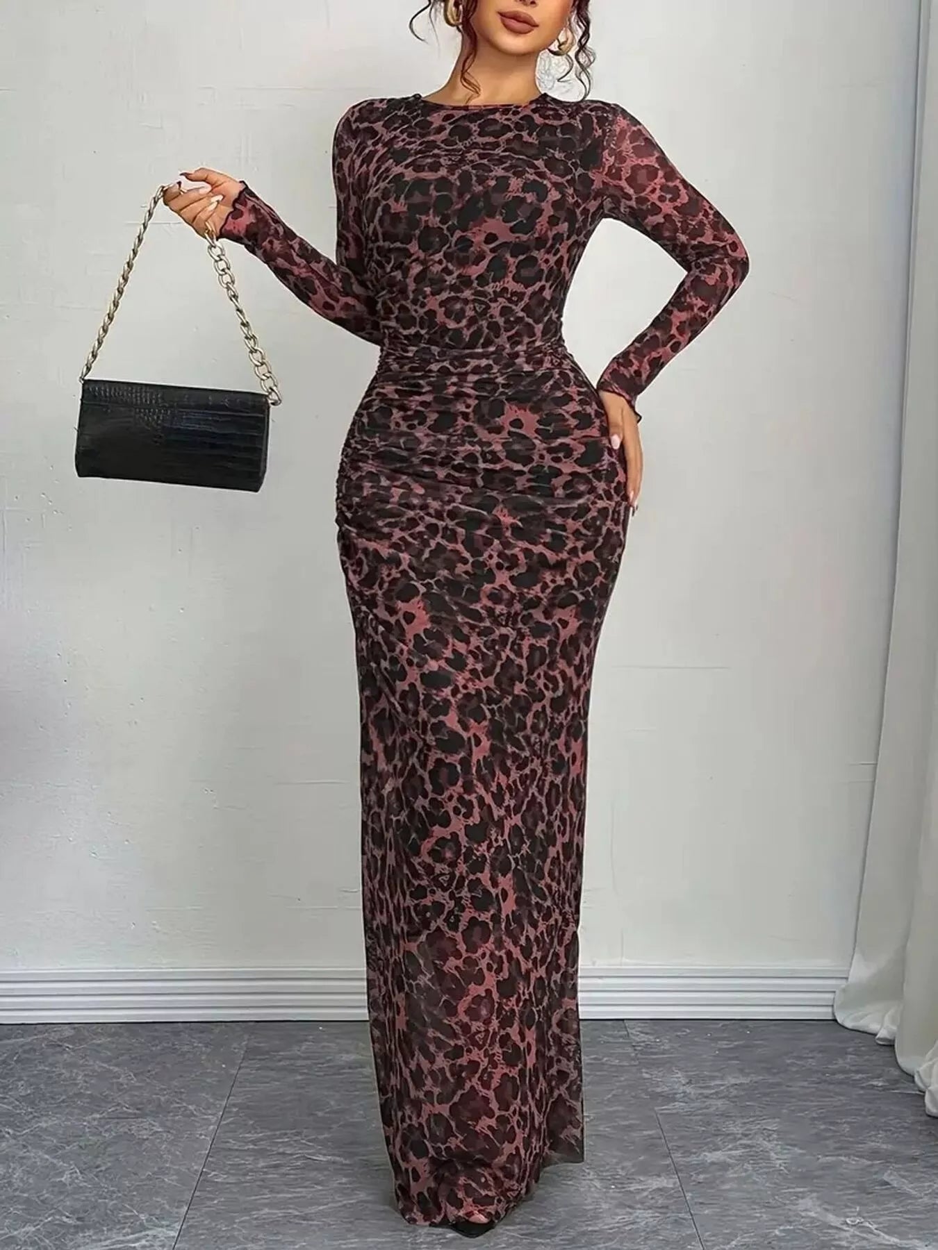 Woman wearing a leopard print dress holding a black handbag against a plain background