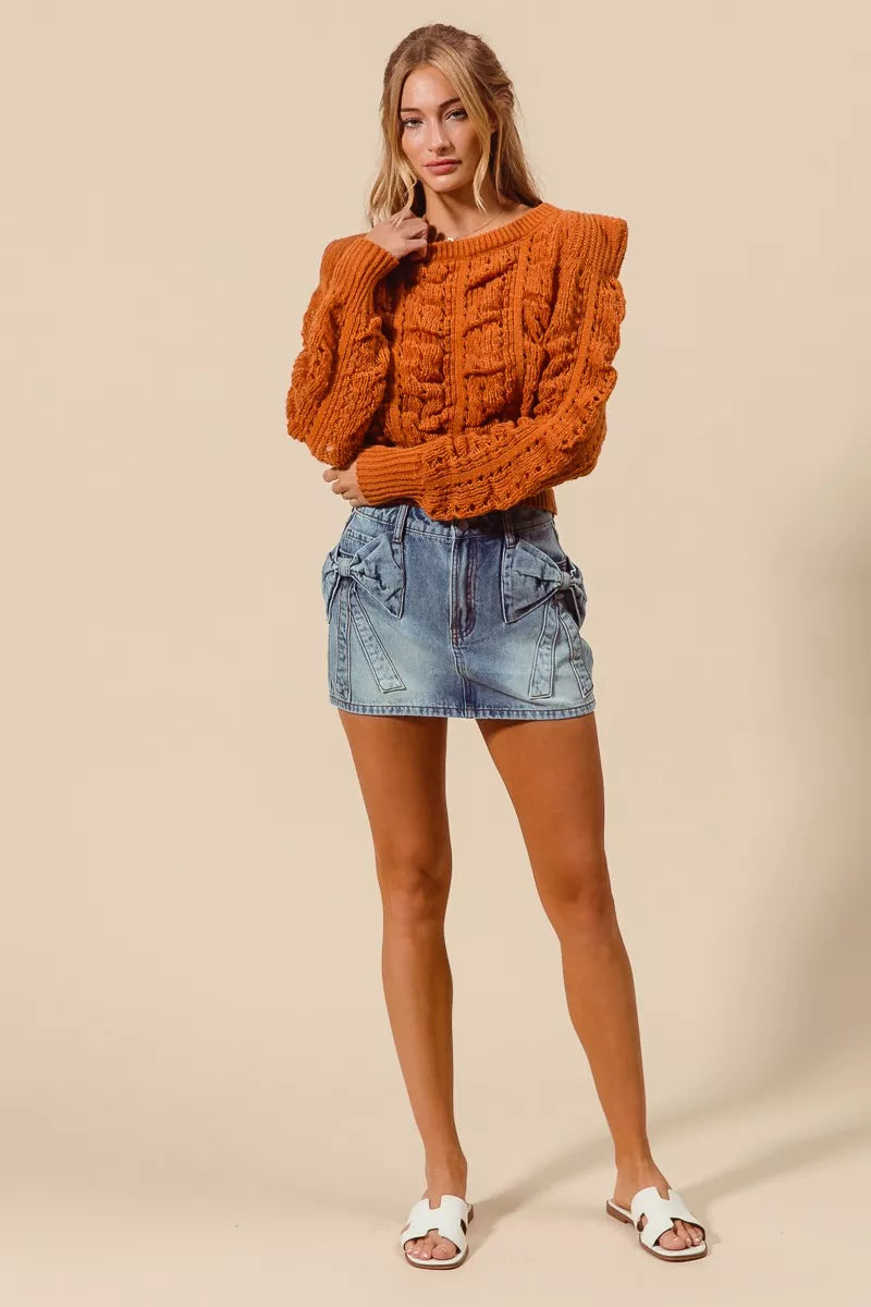 Woman wearing an orange sweater and denim shorts on a beige background