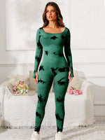 Woman wearing a green and black patterned outfit in a room with white walls and a white couch.