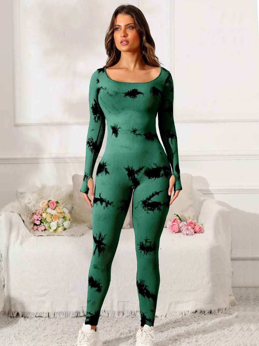 Woman wearing a green and black patterned outfit in a room with white walls and a white couch.