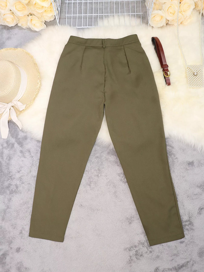 A pair of olive green slim-fit trousers laid flat on a white faux fur surface with decorative props including a straw hat, flowers, a brown belt, and a small purse.