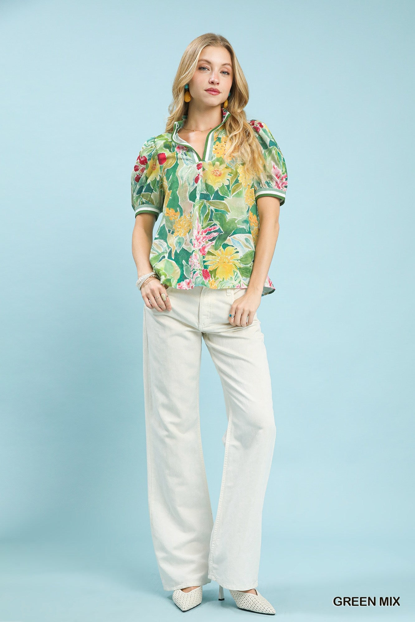 Woman wearing a colorful floral blouse and white pants against a light blue background