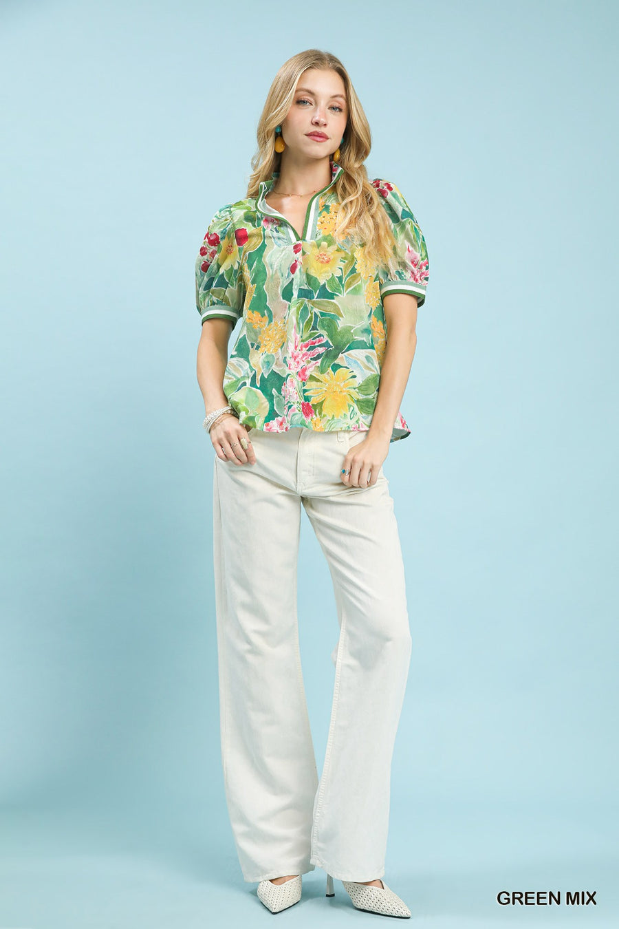 Woman wearing a colorful floral blouse and white pants against a light blue background