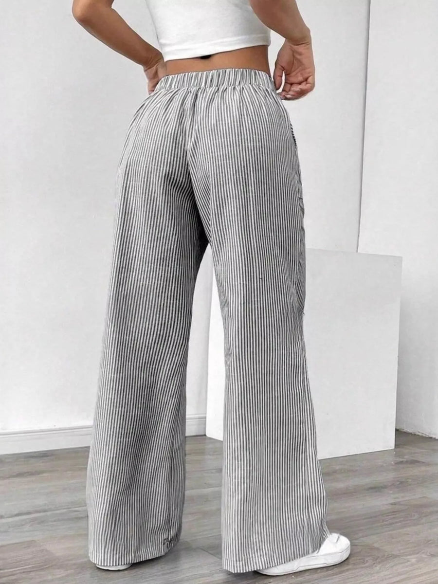 Person wearing gray and white striped wide-leg pants on a plain background