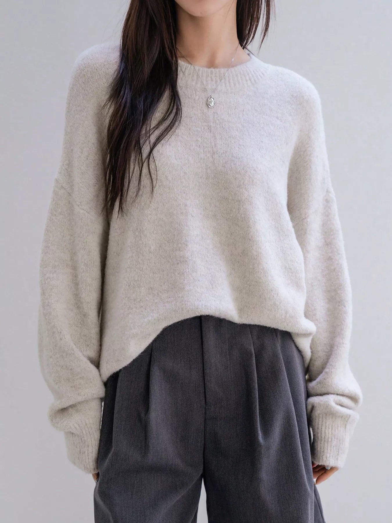 Person wearing a beige sweater and gray pants against a plain background