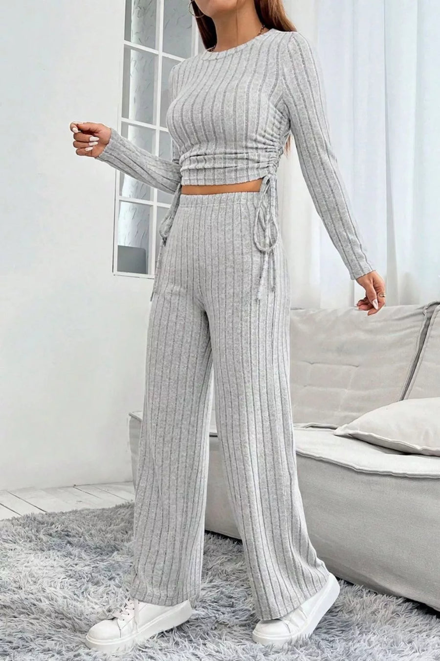 Woman wearing a gray ribbed outfit with a white rug and sofa in the background