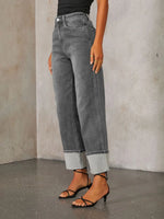 Person wearing gray jeans and black sandals against a plain background