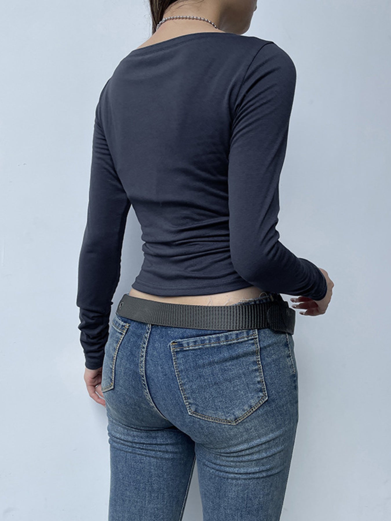 Person wearing a navy long-sleeve top and blue jeans against a light gray background