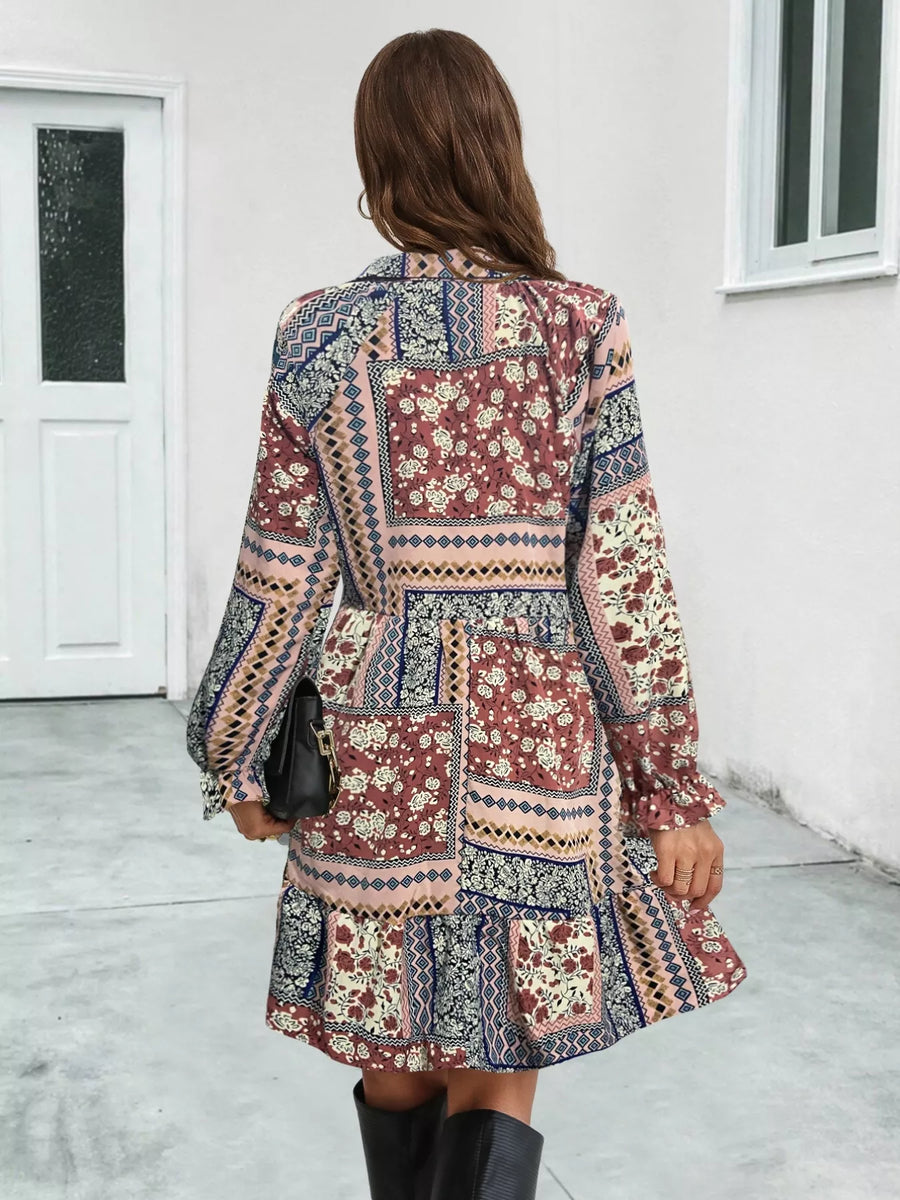 Woman wearing a patterned dress standing in a room with white walls and a door.