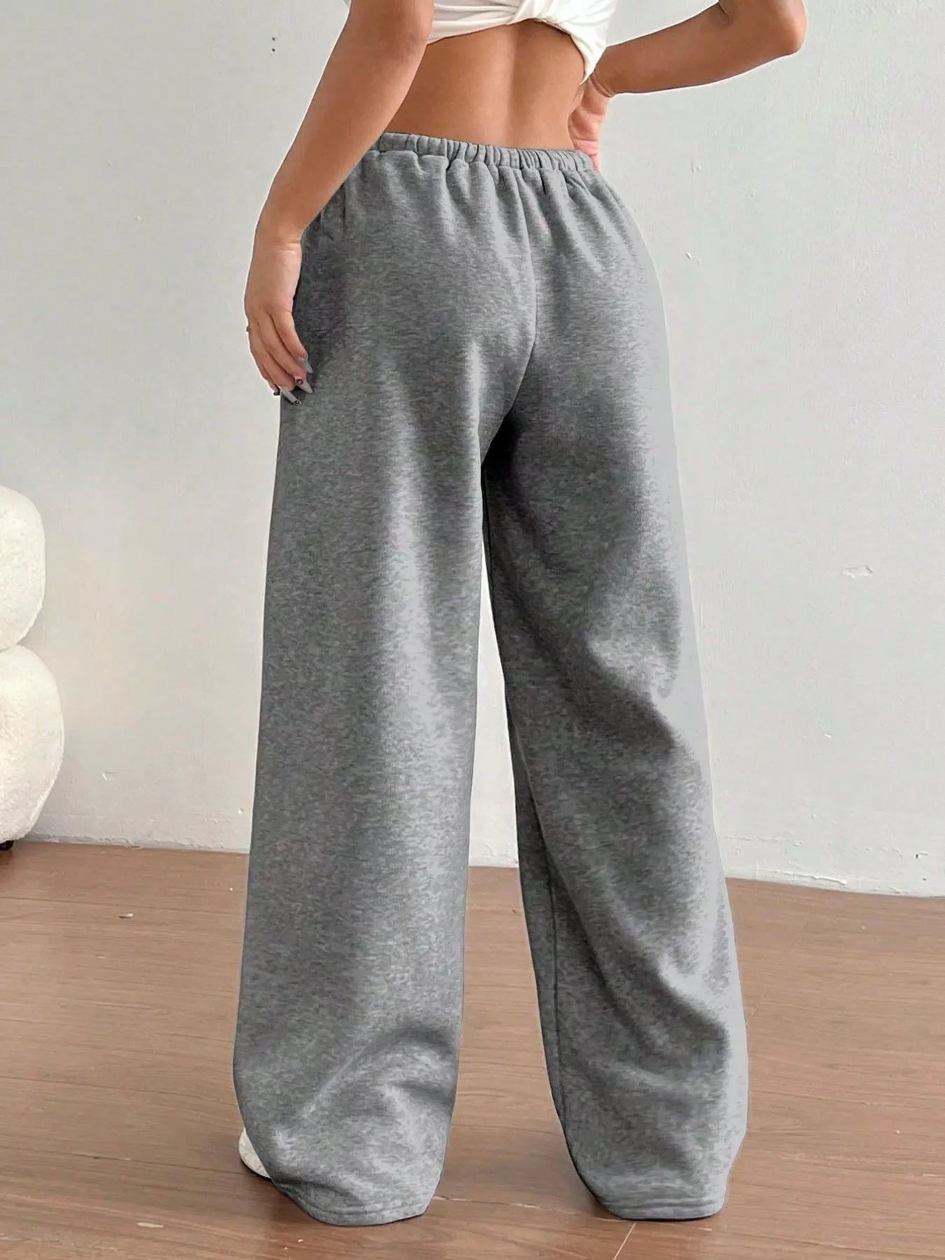 Gray sweatpants worn by a person on a wooden floor with a white wall background
