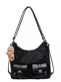 Black handbag with a teddy bear attached to the strap on a white background