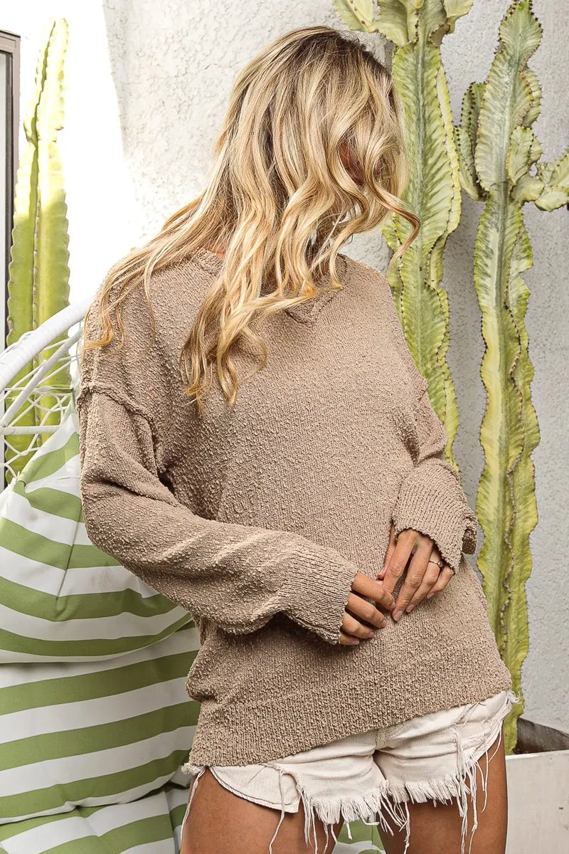 Person wearing a beige sweater and white shorts standing in front of a cactus plant.