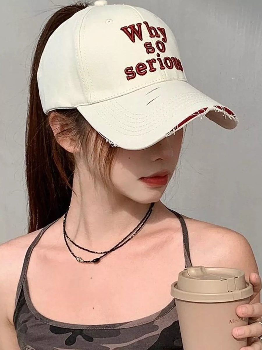 Person wearing a cap with 'Why so serious' text and holding a coffee cup.