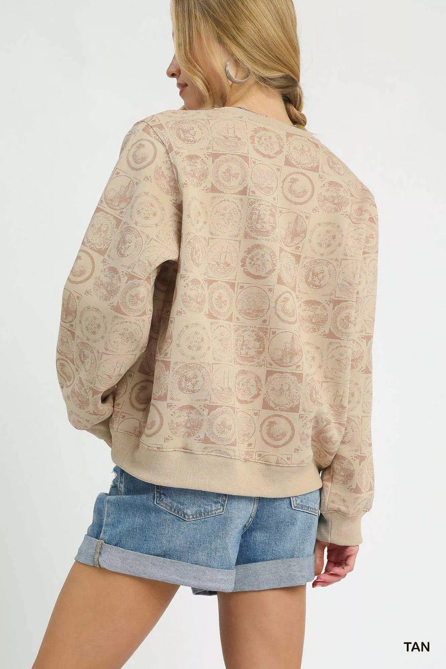 Woman wearing a beige patterned sweater and denim shorts on a white background