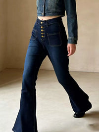 Person wearing dark blue flared jeans and a denim jacket on a neutral background