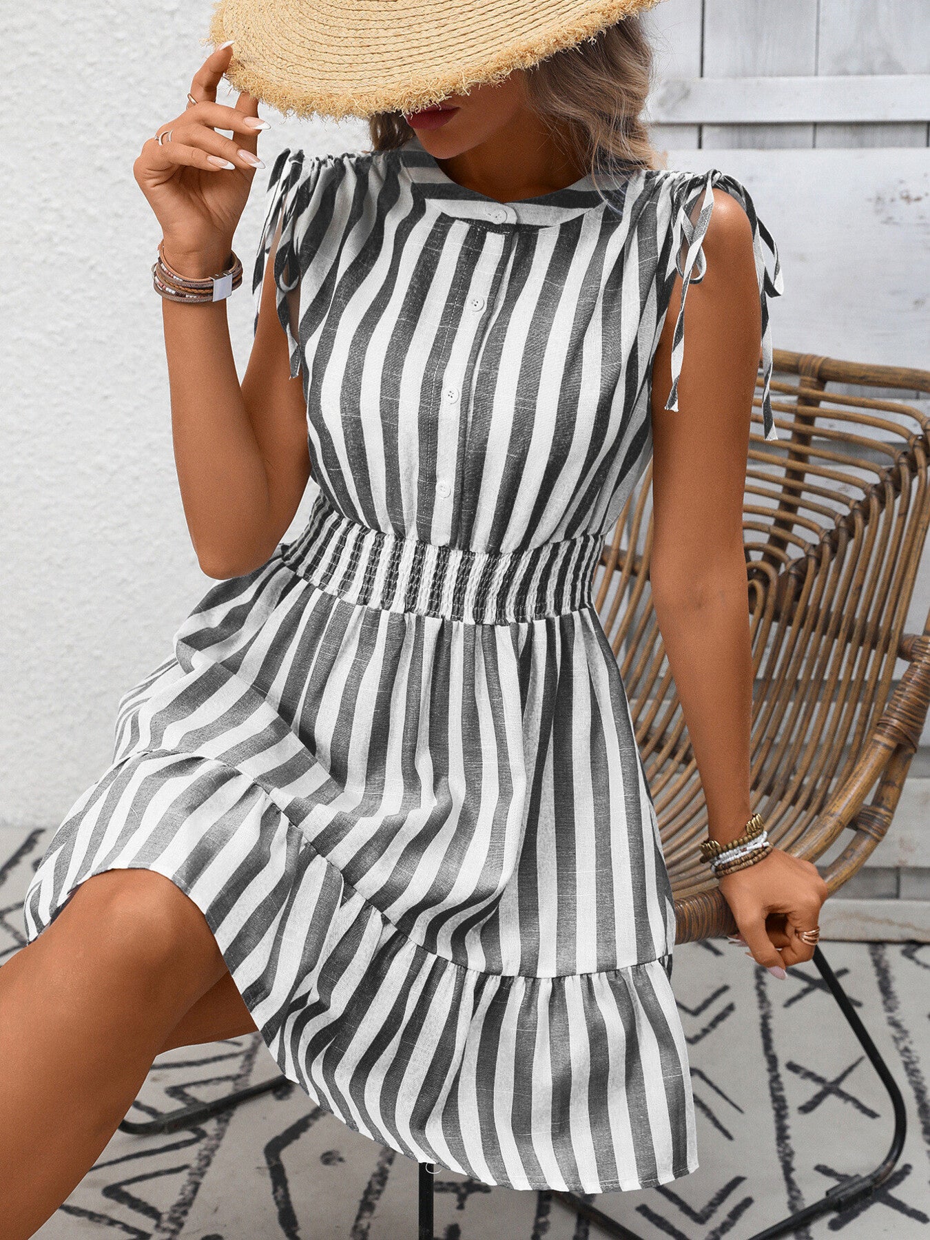 Woman wearing a black and white striped dress with a straw hat, standing against a light wooden wall.