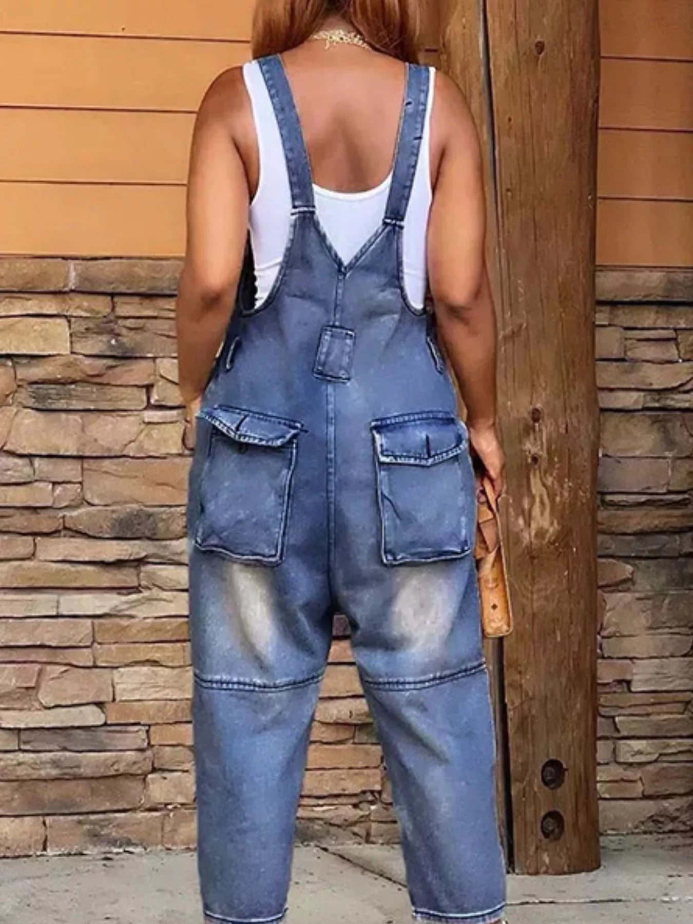 Person wearing blue denim overalls standing against a stone wall.