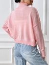 Person wearing a pink sweater and light blue jeans against a white wall.