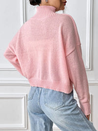 Person wearing a pink sweater and light blue jeans against a white wall.