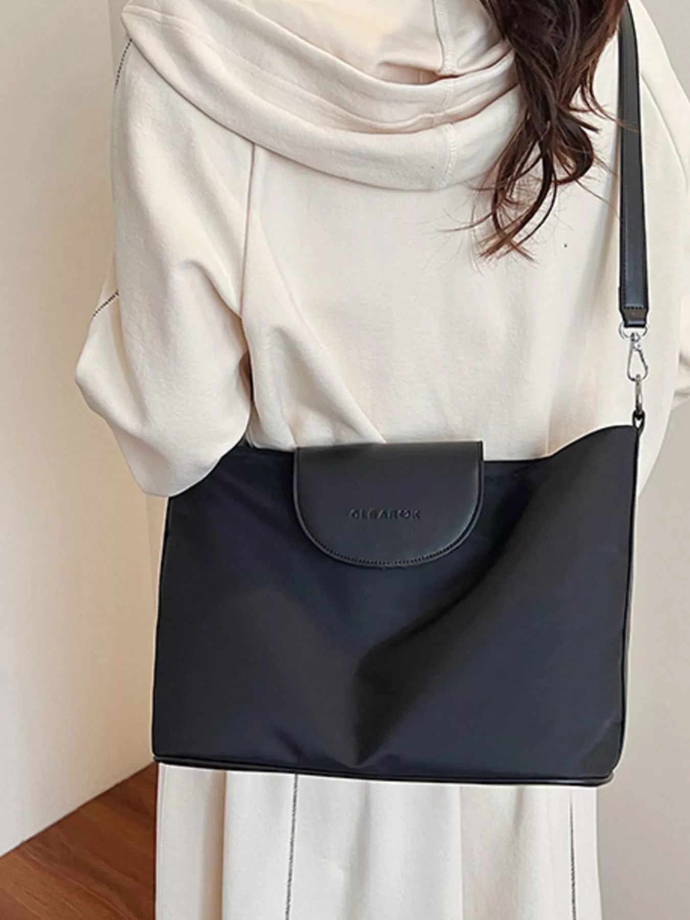 Person wearing a black shoulder bag with a neutral background