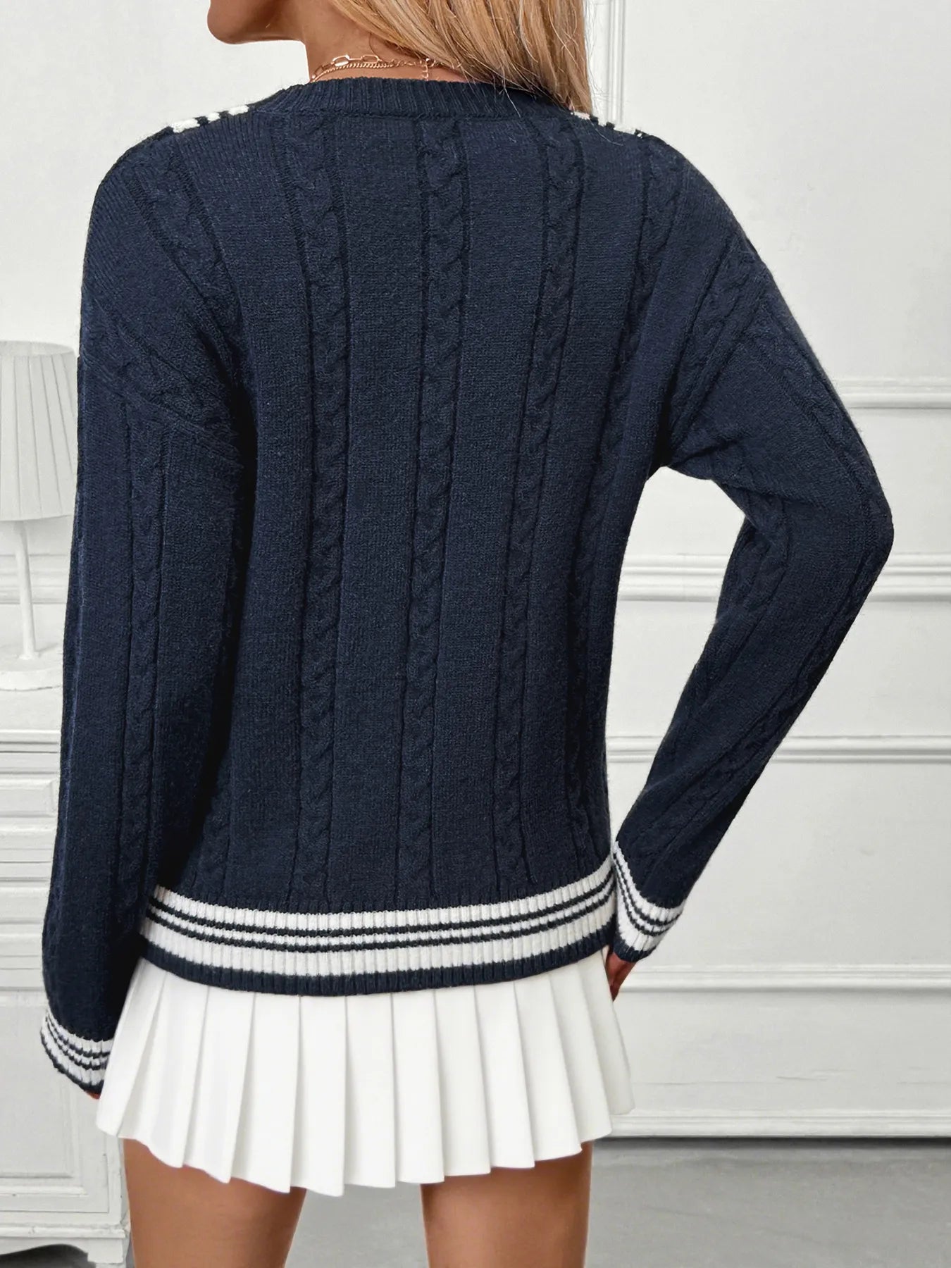 Navy blue cable knit sweater with white trim worn by a person on a white background