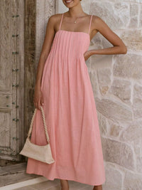 Woman wearing a pink dress standing against a stone wall.