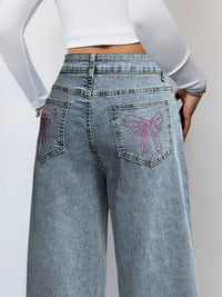 Light blue jeans with pink butterfly designs on the pockets against a plain background