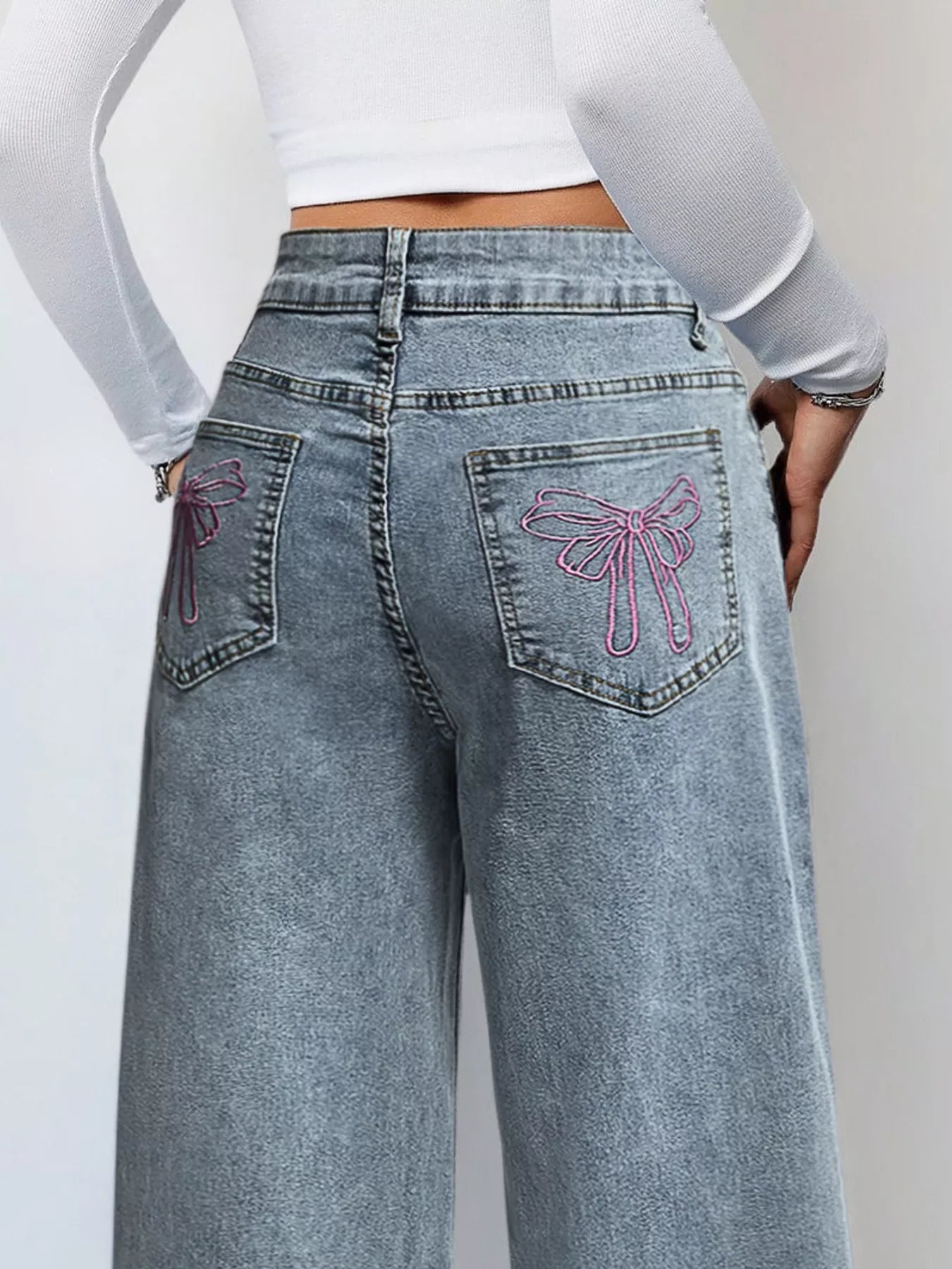 Light blue jeans with pink butterfly designs on the pockets against a plain background