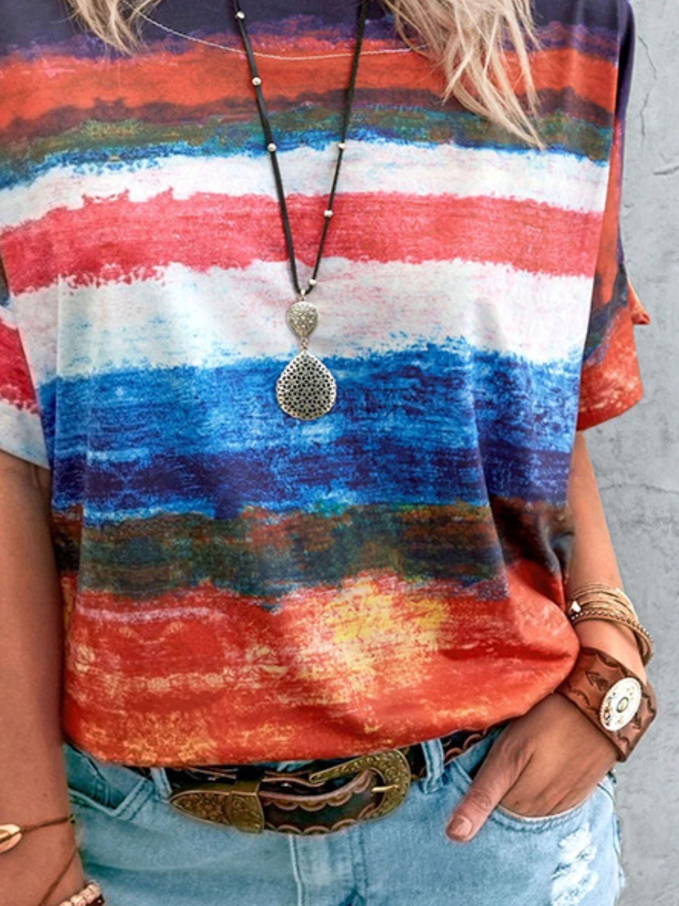 Person wearing a colorful striped shirt with a necklace and bracelet on a gray background