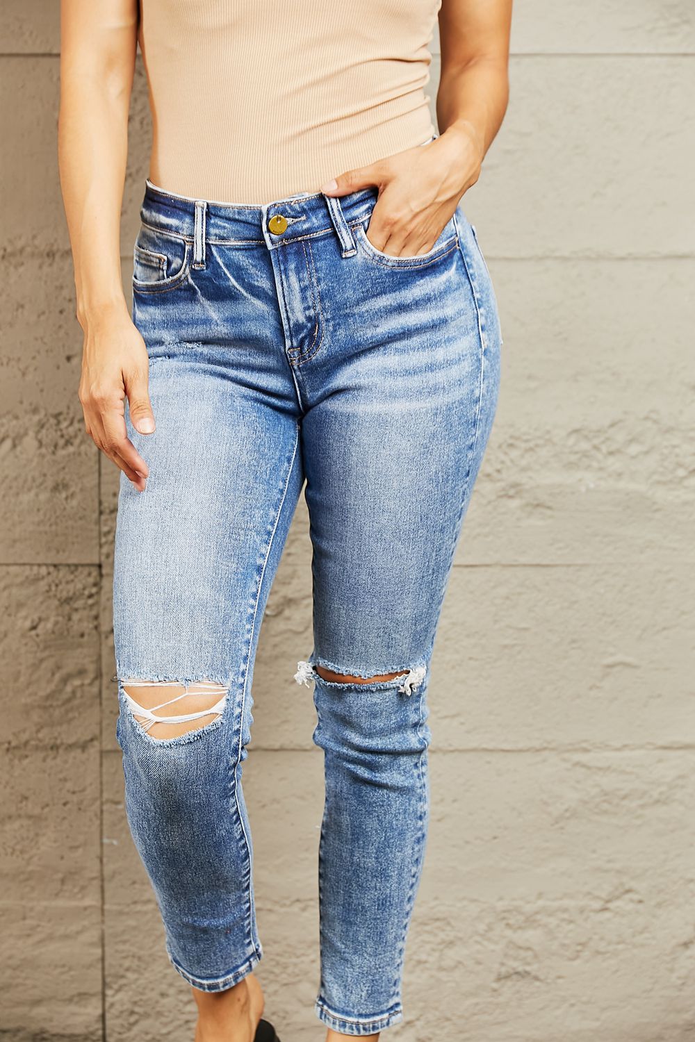 Person wearing light blue ripped jeans against a beige wall