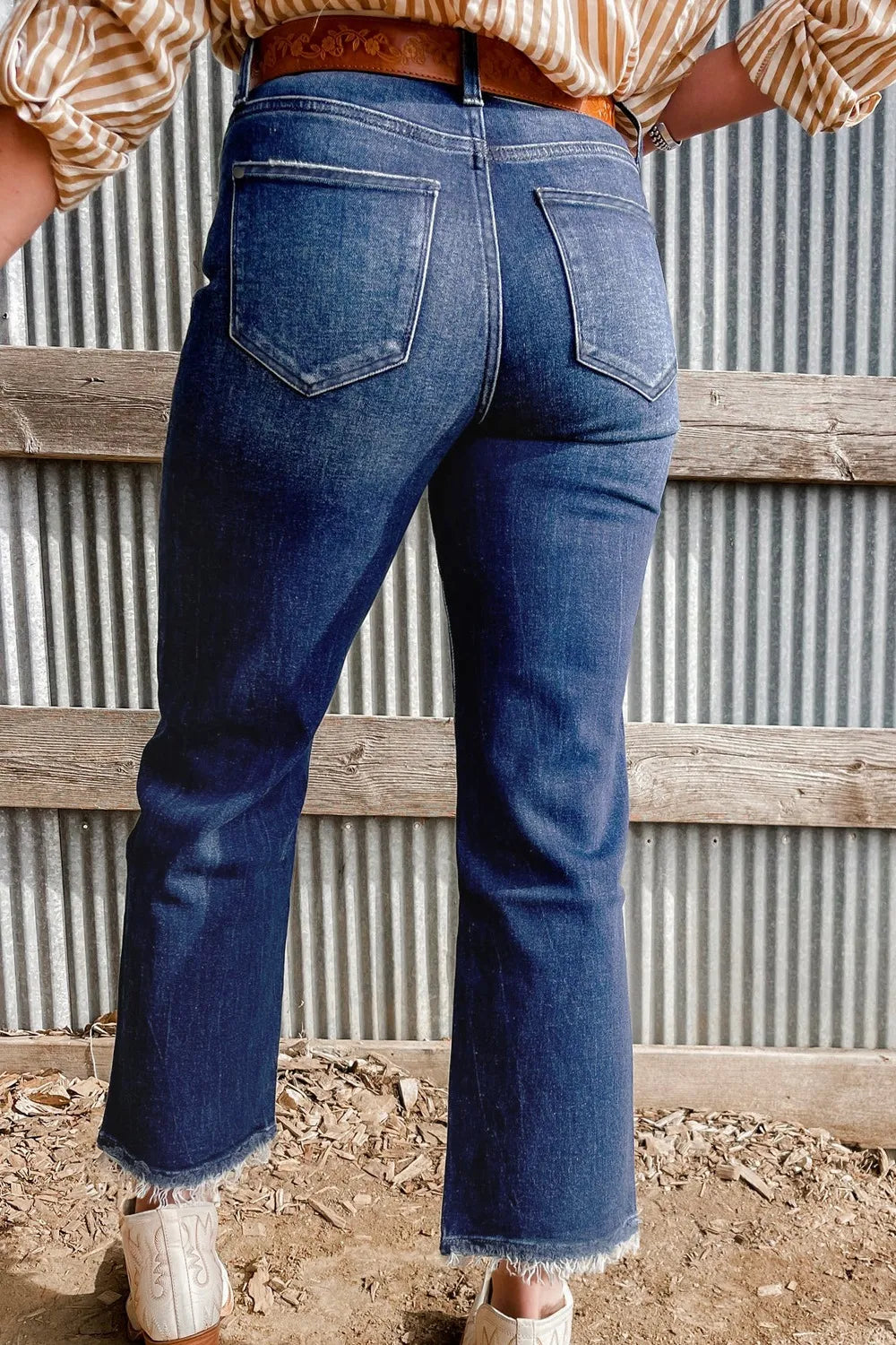 Person wearing blue jeans with a rustic wooden and metal fence background