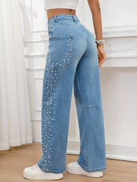 Person wearing blue jeans with rhinestone embellishments in a room with white walls and wooden floor.