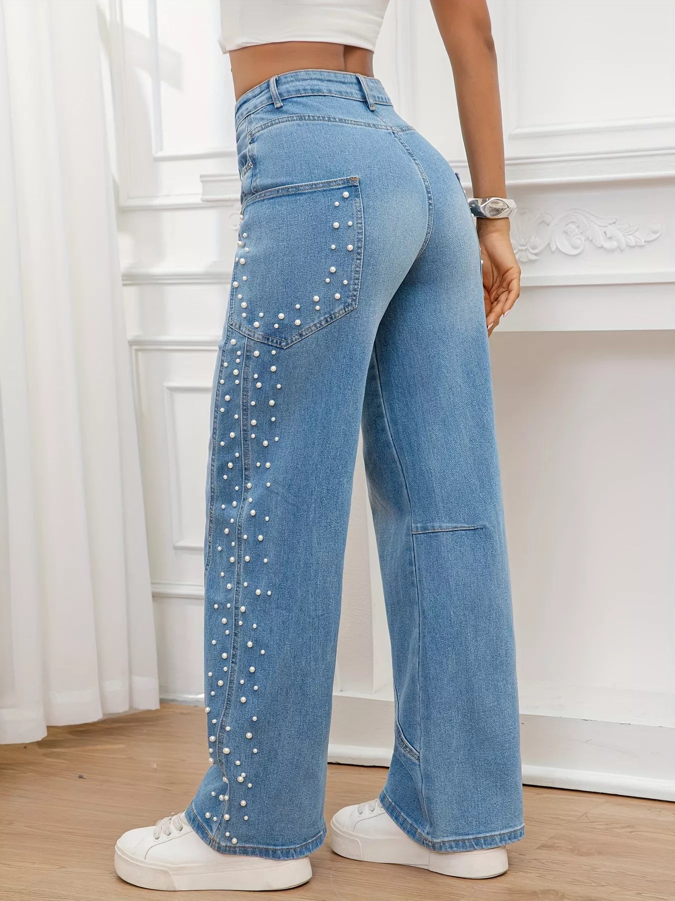 Person wearing blue jeans with rhinestone embellishments in a room with white walls and wooden floor.