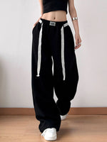 Person wearing black baggy pants with white drawstrings on a plain background