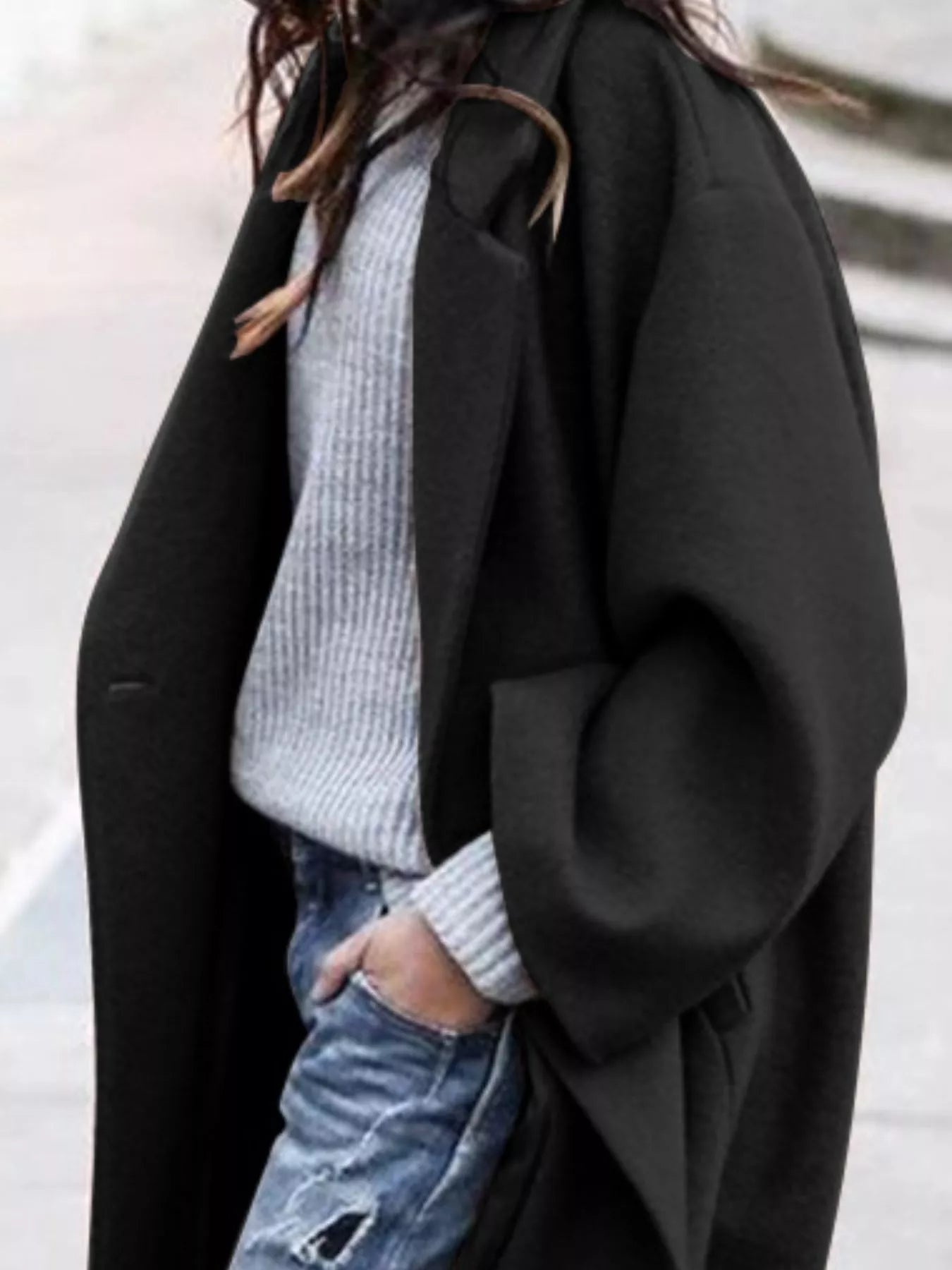 Person wearing a black coat over a light gray sweater and blue jeans.