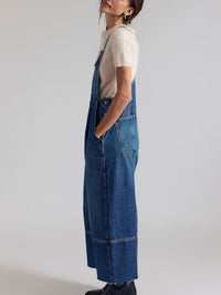 Person wearing a blue denim overall dress on a plain background
