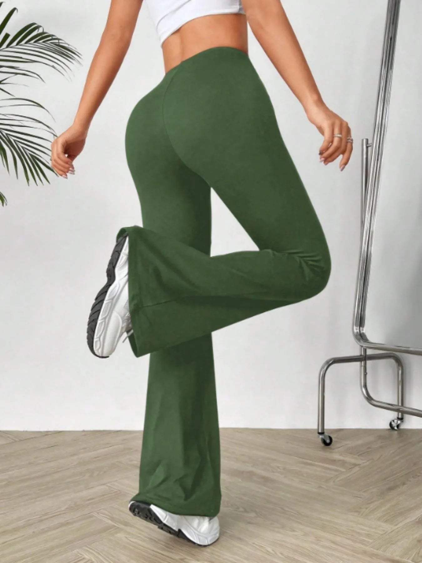 Person wearing green high-waisted leggings and white sneakers on a plain background