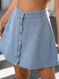 Light blue denim skirt with button details worn by a person on a blurred street background