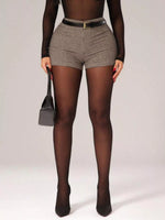 Person wearing checkered shorts, black tights, and high heels on a plain background
