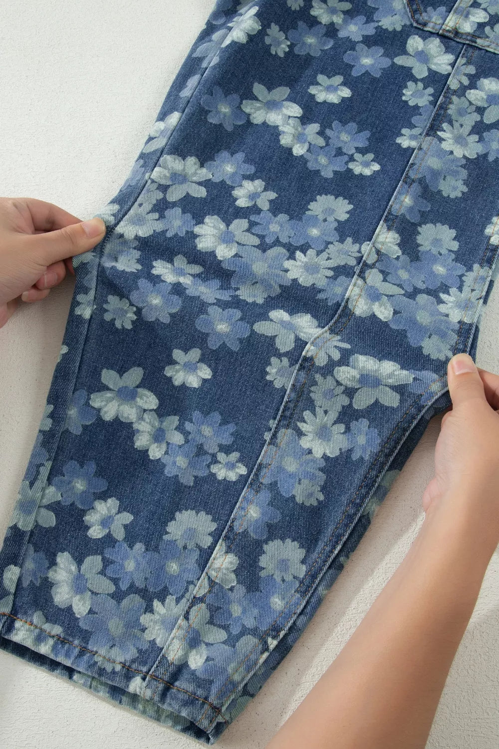 Blue floral-patterned denim fabric being held by hands on a white background