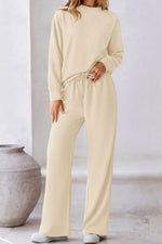 Person wearing a beige lounge set in a minimalistic setting with a vase.