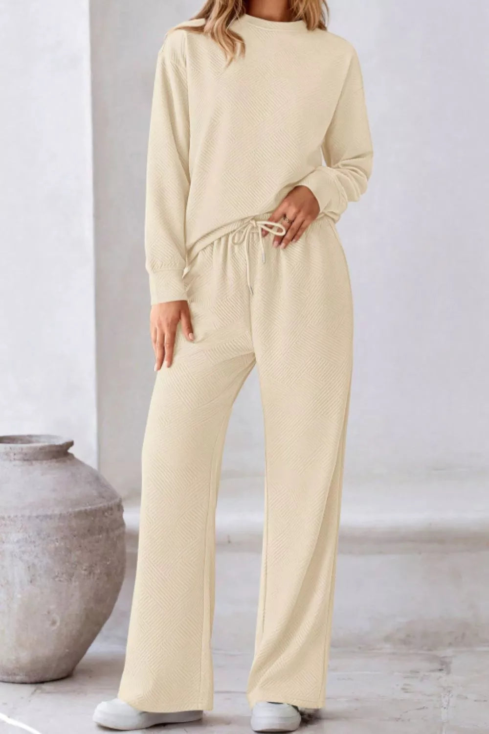 Person wearing a beige lounge set in a minimalistic setting with a vase.