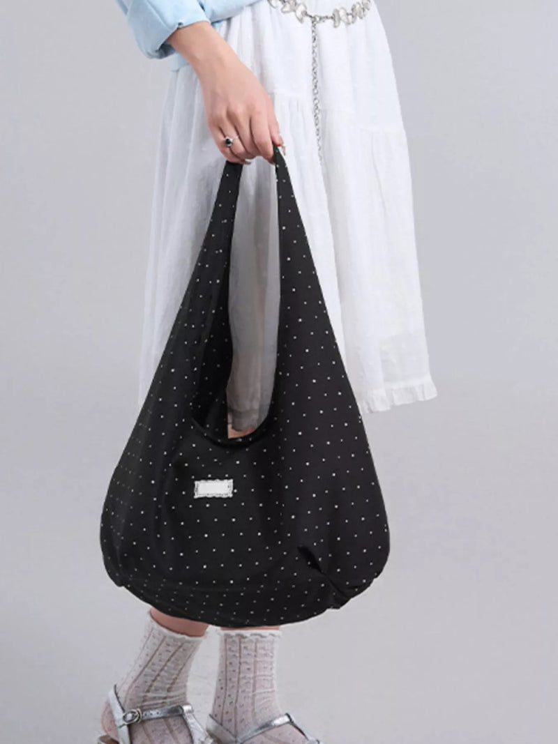 Person holding a black polka dot bag against a plain background