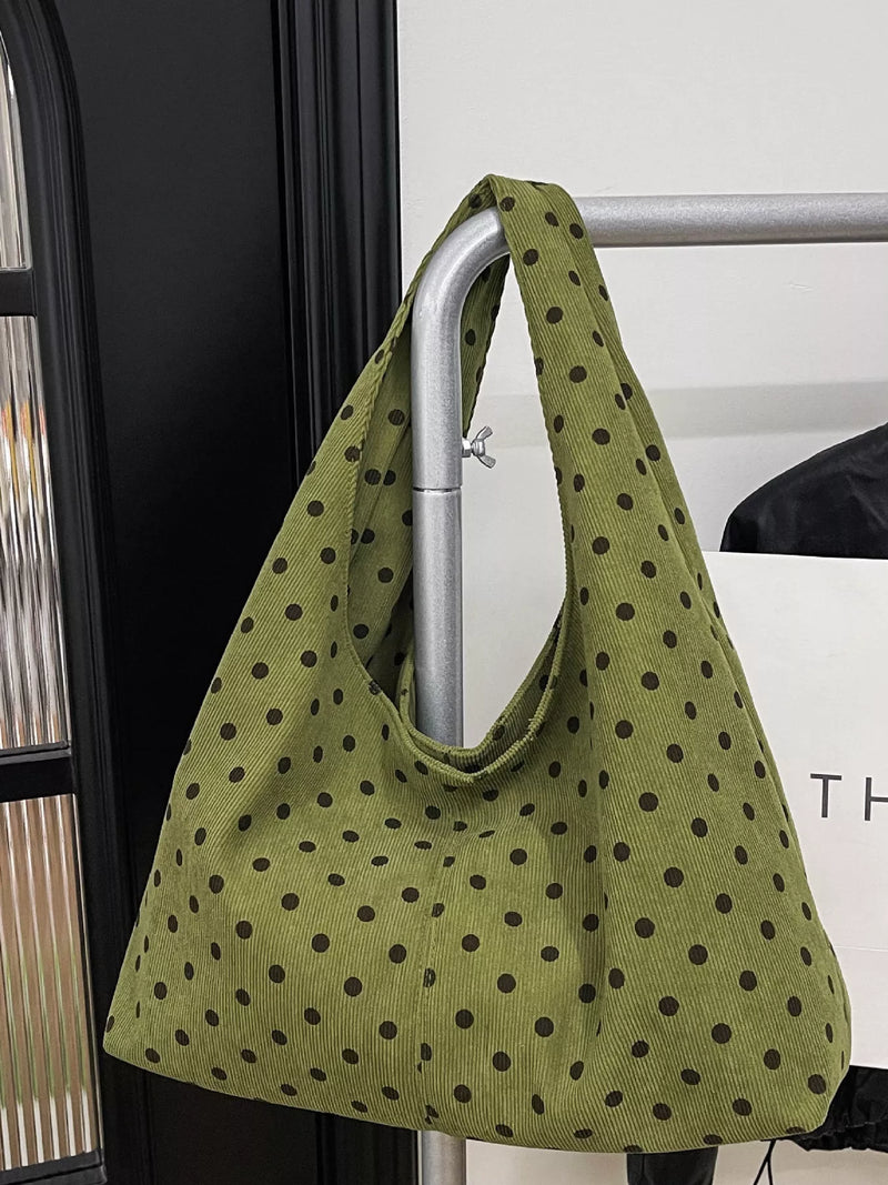 An olive green canvas shoulder bag with a dark brown polka dot pattern, hanging from a silver metal clothing rack.