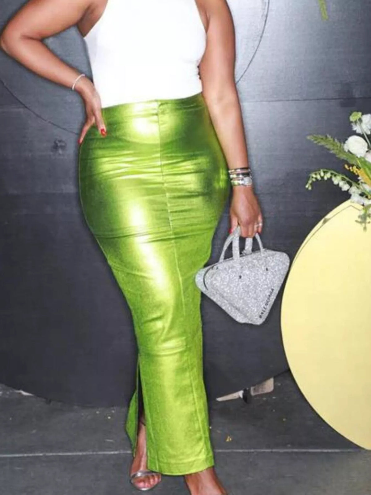 Person wearing a green metallic skirt with a white top and silver shoes, standing against a dark background.