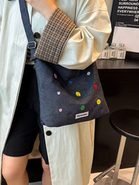 Person holding a denim bag with colorful patches in an indoor setting