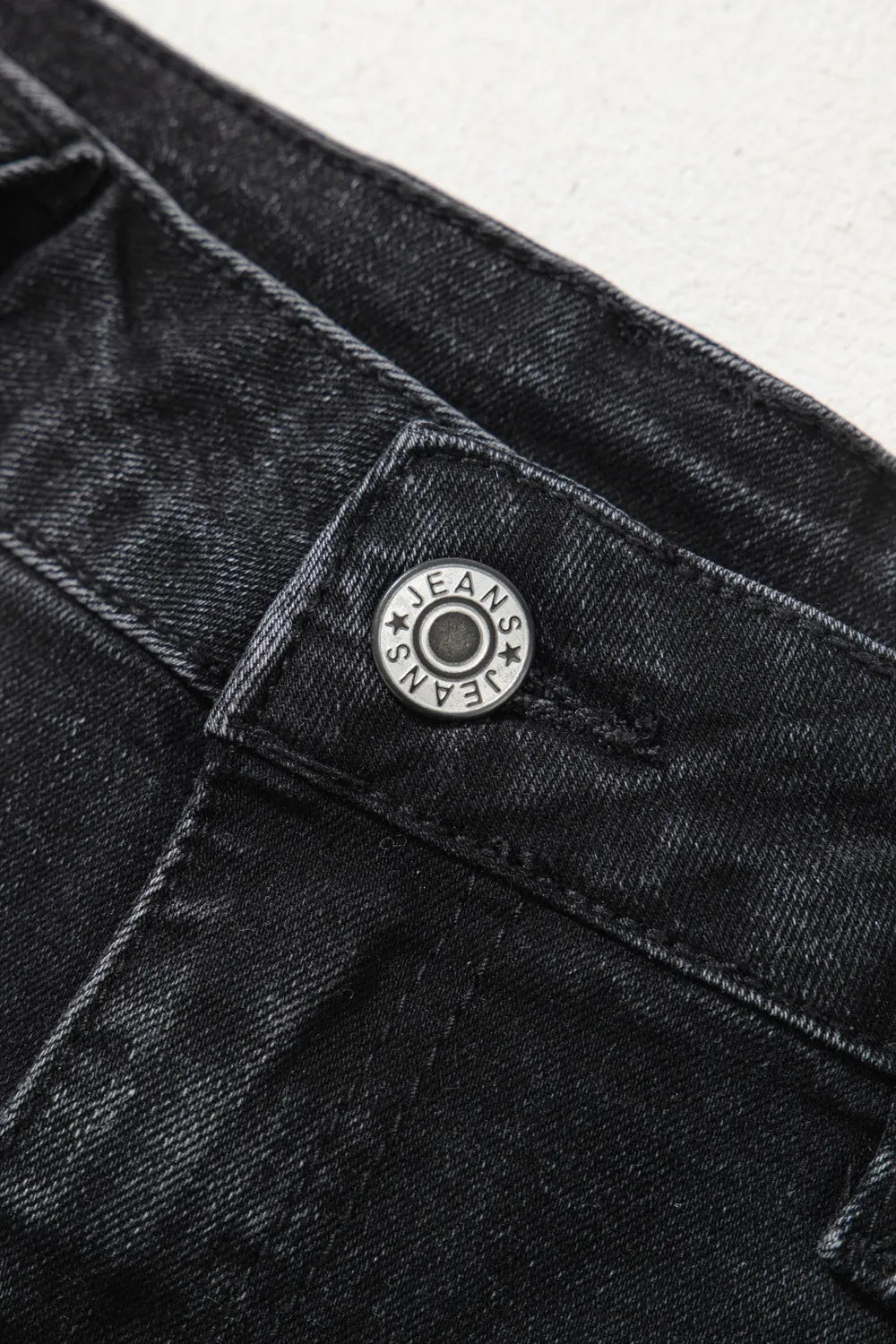 Close-up of a black denim button with 'EAM' branding on a white background