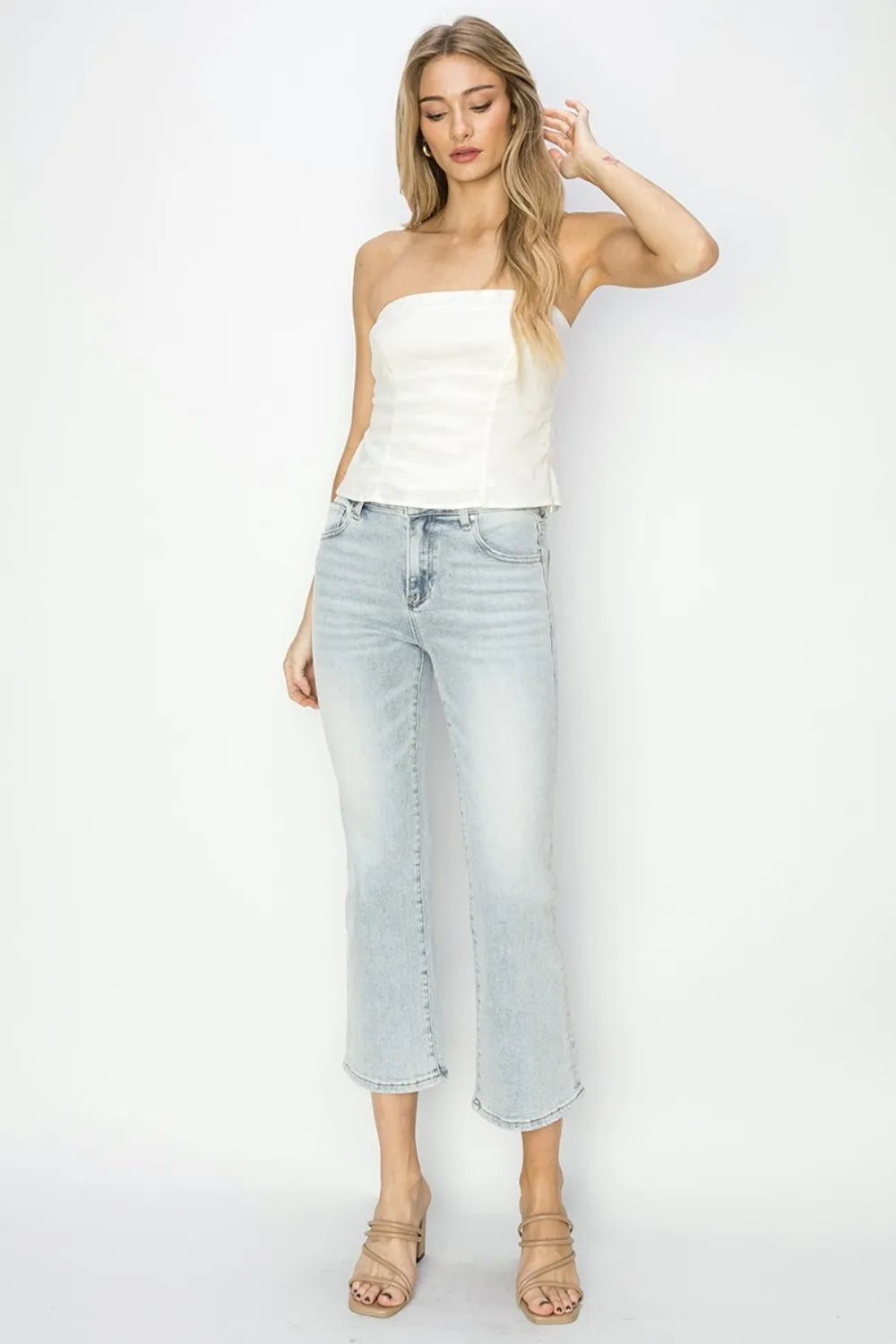 Woman wearing a white strapless top and light blue jeans on a white background