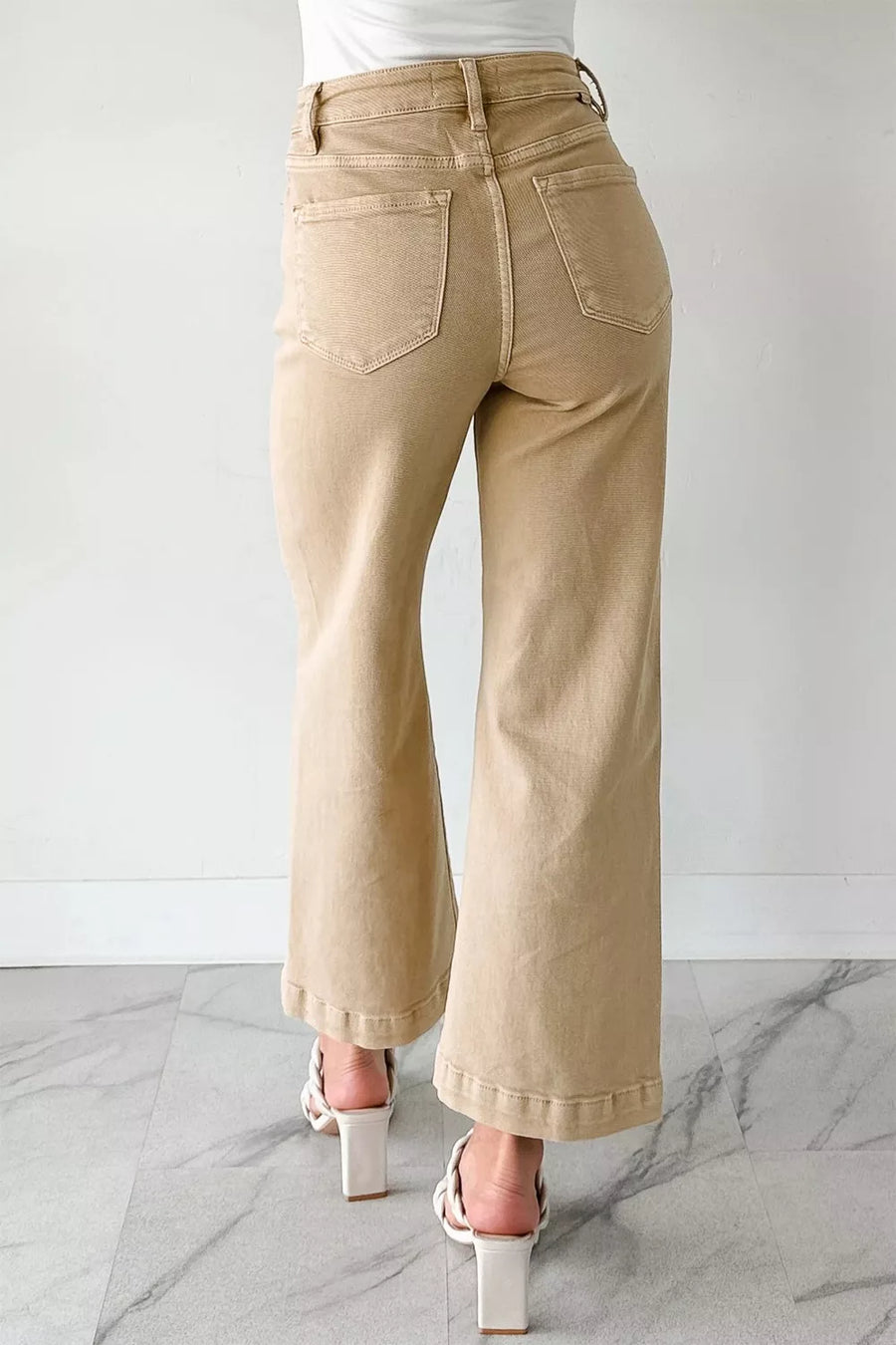 Beige wide-leg pants worn by a person on a marble floor with a white background