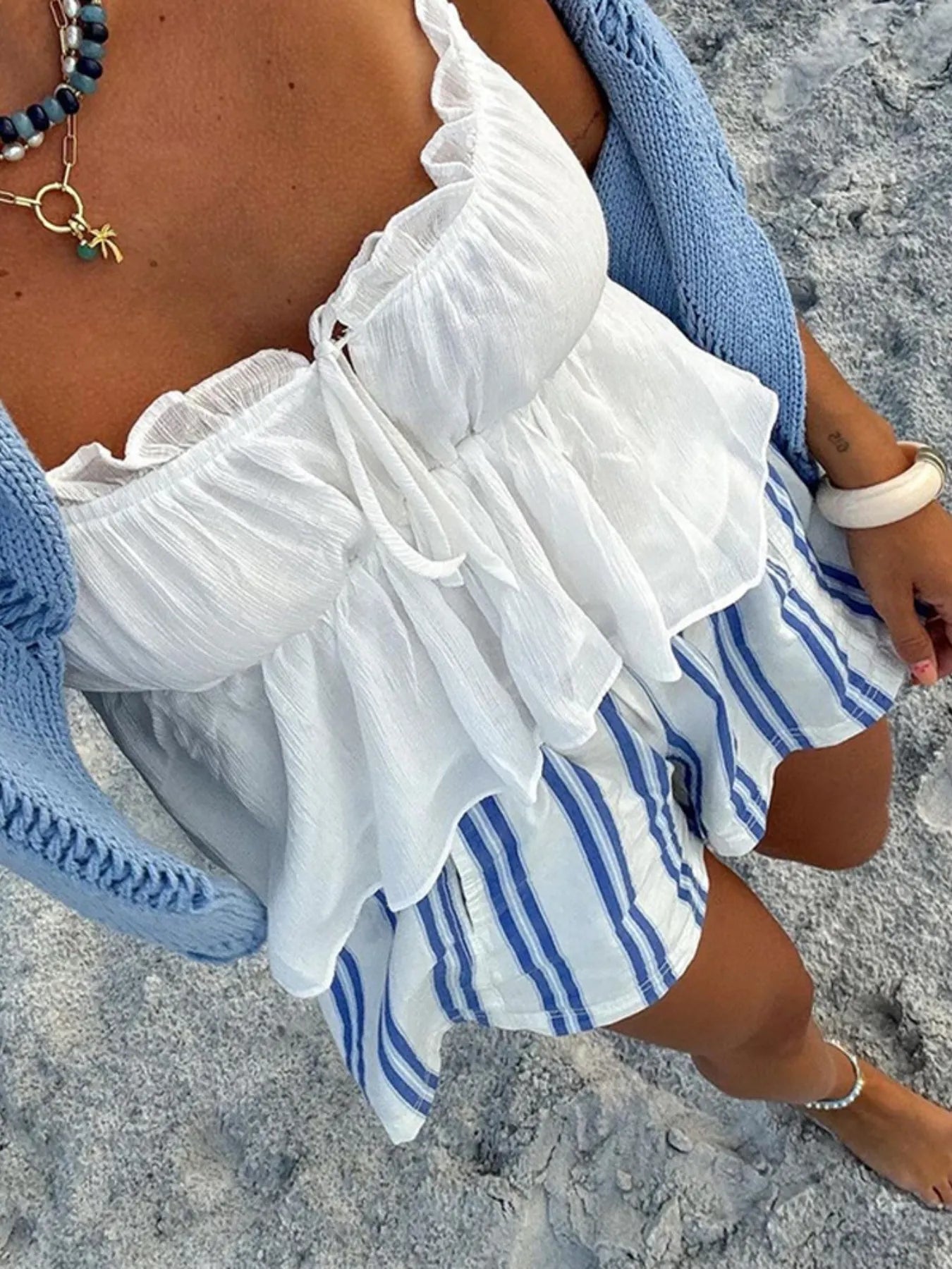 Person wearing a white top with ruffles and blue striped shorts on a sandy surface